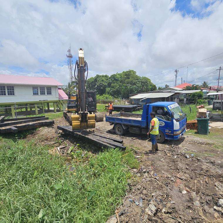 Excavator-mounted pile driver beside timber and sheet piles